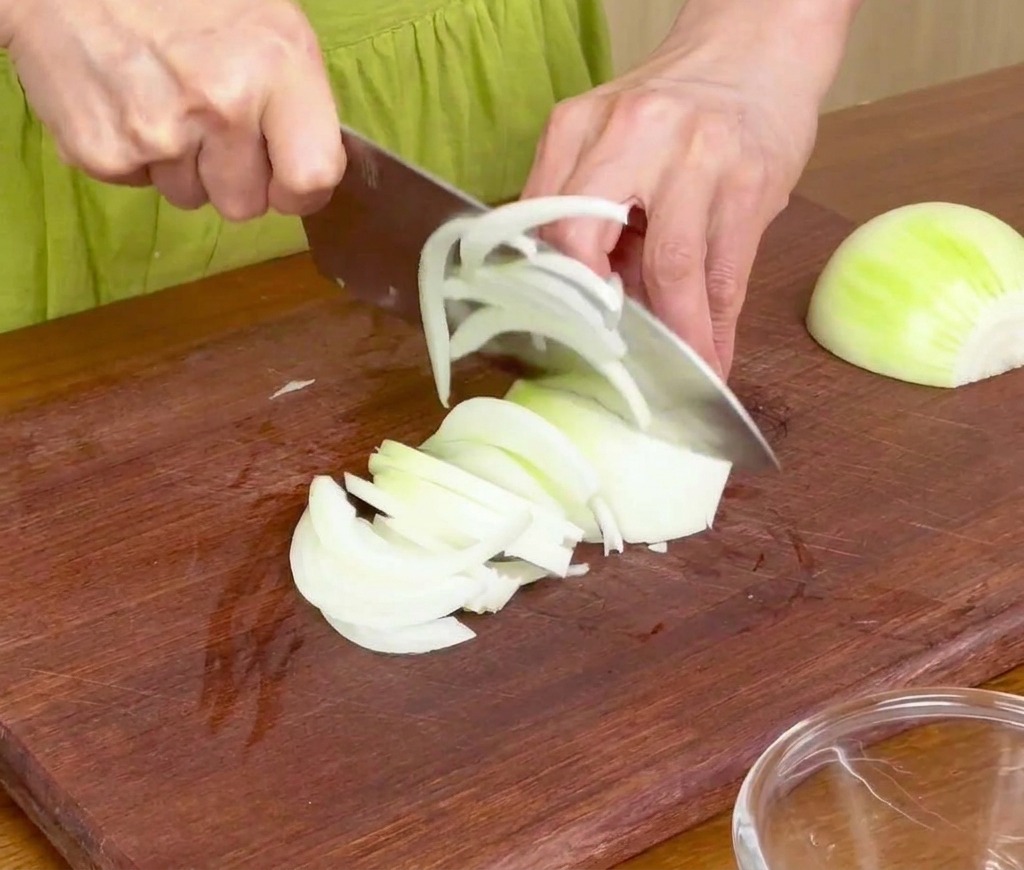 Cortando cebollas blancas en tiras finas sobre una tabla de cortar de madera con un cuchillo de chef.
