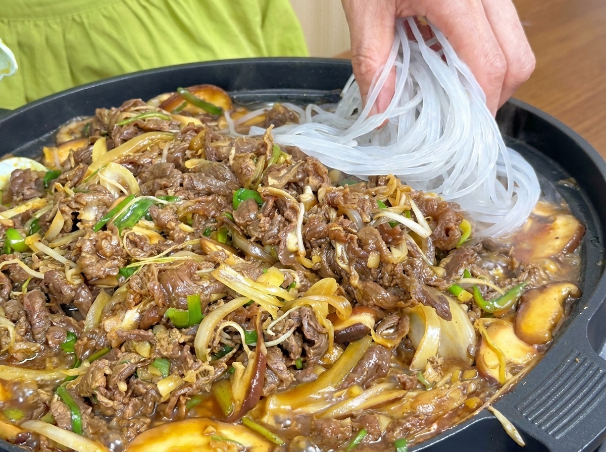 Fideos de cristal translúcidos que se añaden a la sartén con la carne y las verduras cocinándose.