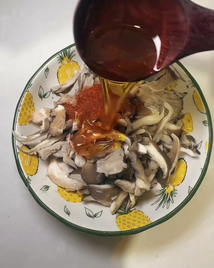 Aceite de cocina siendo vertido desde una cuchara de madera sobre el chile y las setas.