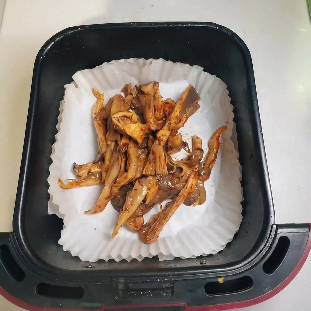 Setas sazonadas extendidas en una cesta de freidora de aire forrada con papel de horno.
