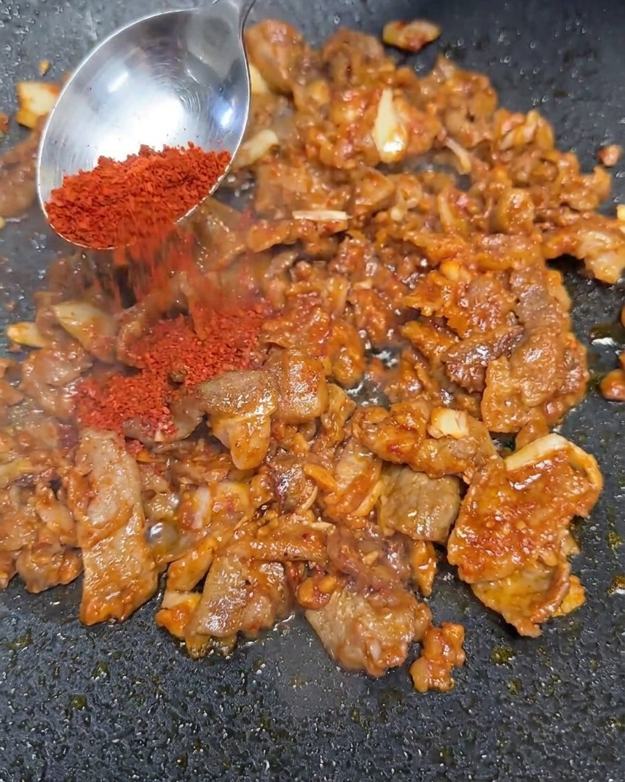 Chile rojo en polvo añadiéndose a la mezcla de carne sofrita.