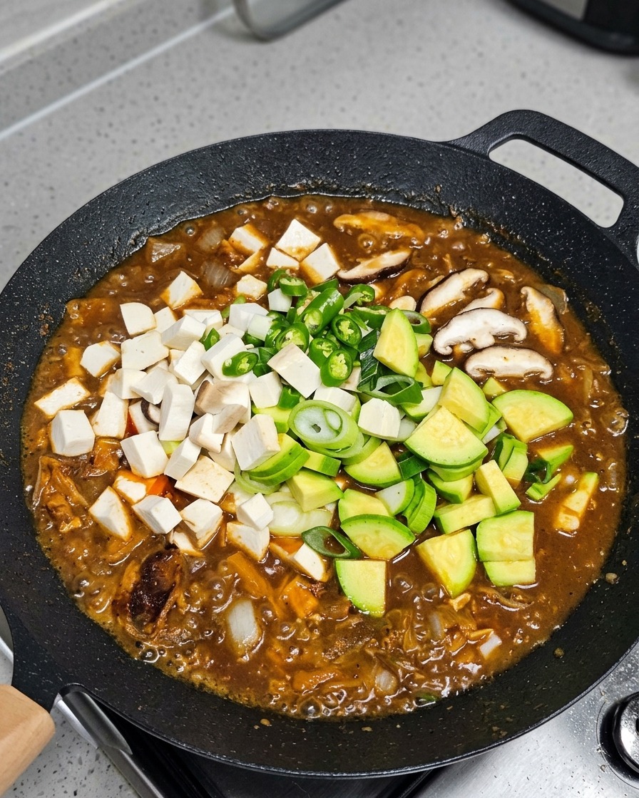 Verduras y tofu incorporándose al estofado hirviendo a fuego lento.