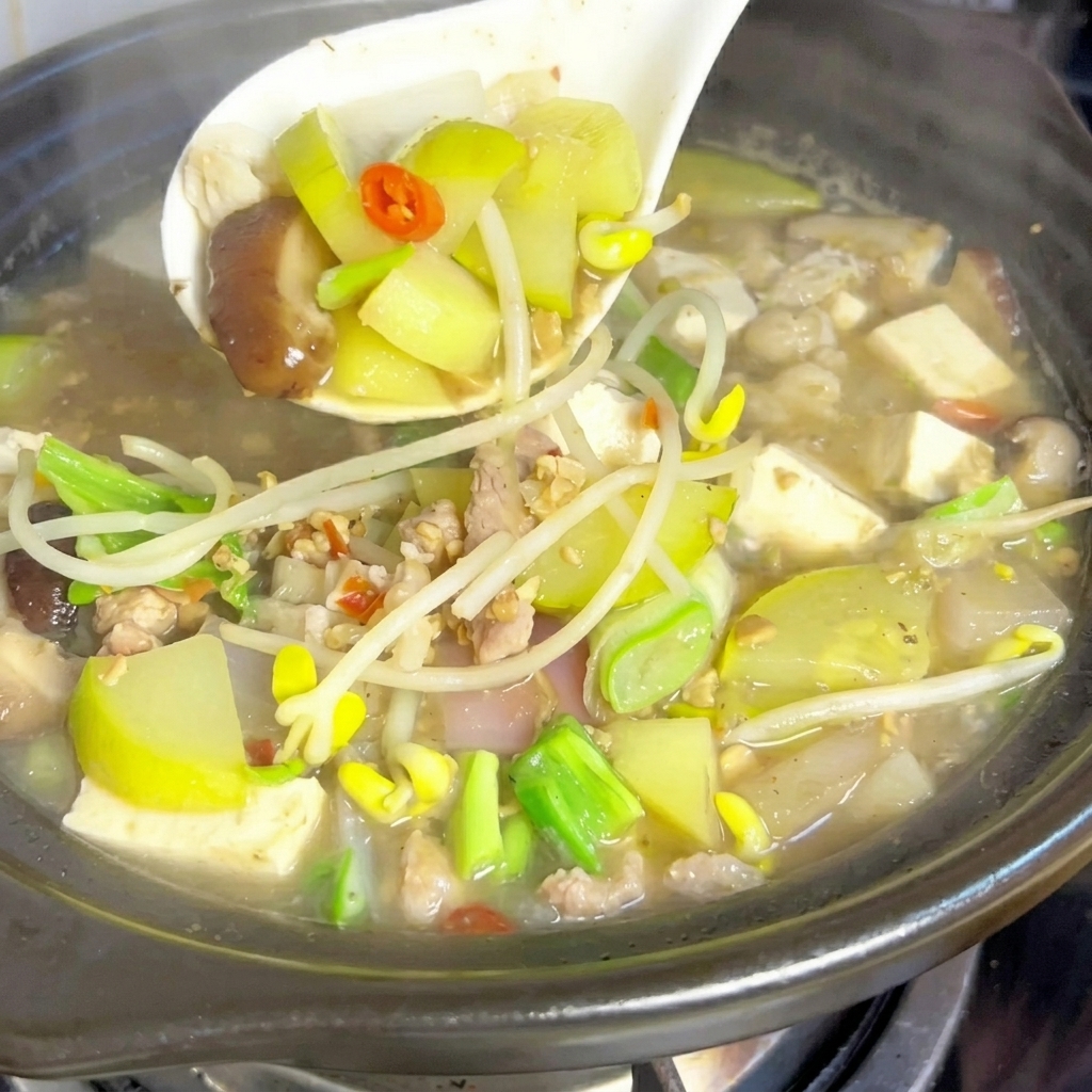 Una cuchara de metal mezclando una porción generosa de pasta de soja fermentada en el caldo burbujeante del estofado.