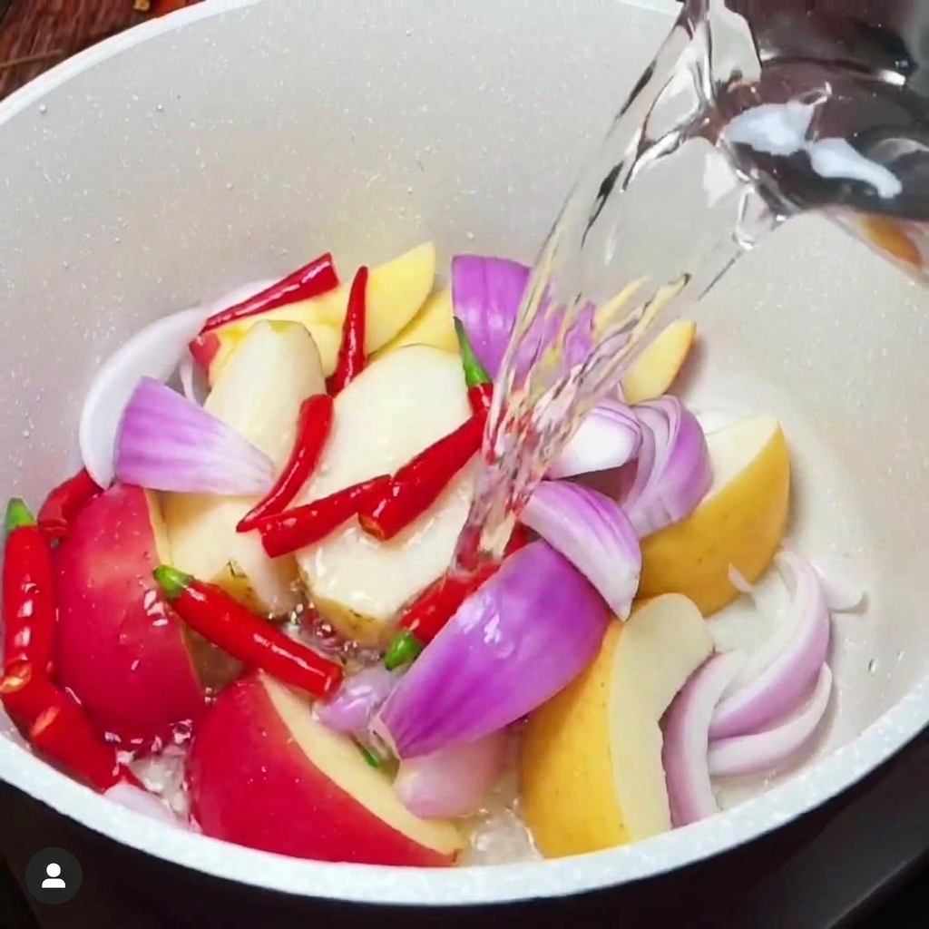 Condimentos líquidos vertiéndose en una olla blanca con una mezcla de frutas y verduras picadas.