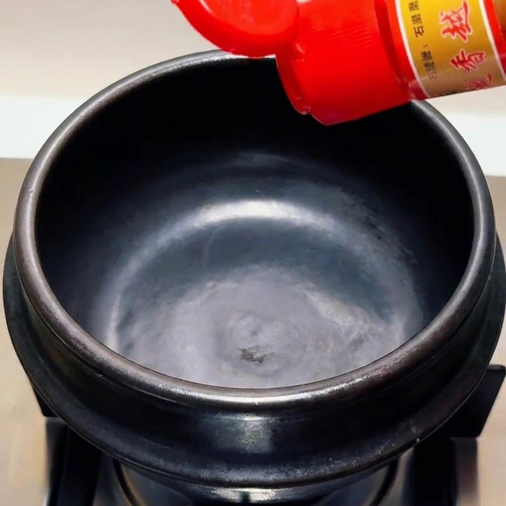 Aceite de sésamo vertido desde una botella con tapa roja en una olla de piedra negra vacía.