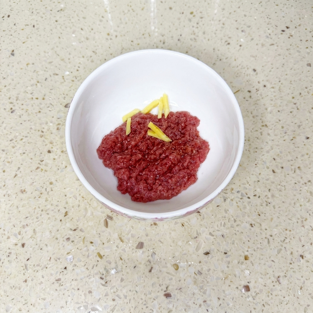 Carne picada en un bol blanco mezclada con salsa de soja, aceite y maicena, decorada con rodajas de jengibre.