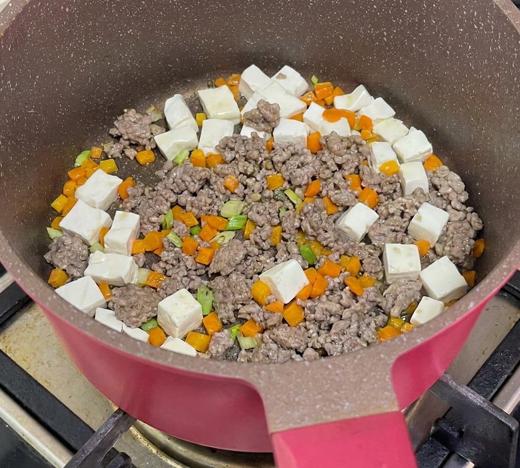 Agua hirviendo siendo vertida en la sartén con tofu, carne y zanahorias para cocinar a fuego lento.