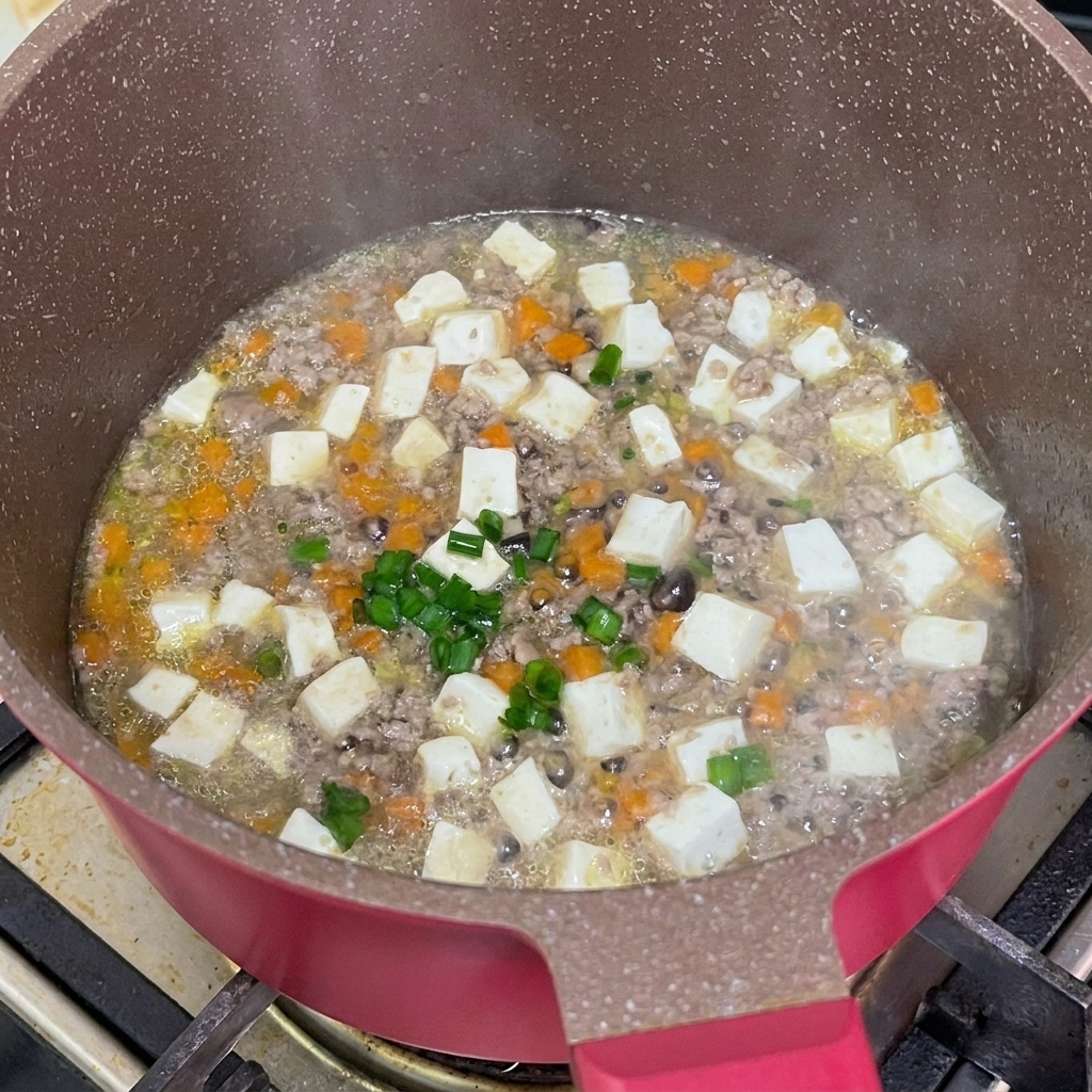 Cebollino fresco picado espolvoreado sobre el guiso de ternera y tofu en la sartén.