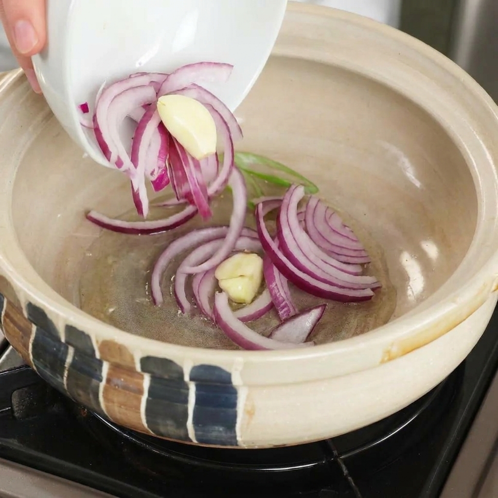 Cebolla morada y ajos laminados siendo añadidos a una cazuela caliente con aceite.