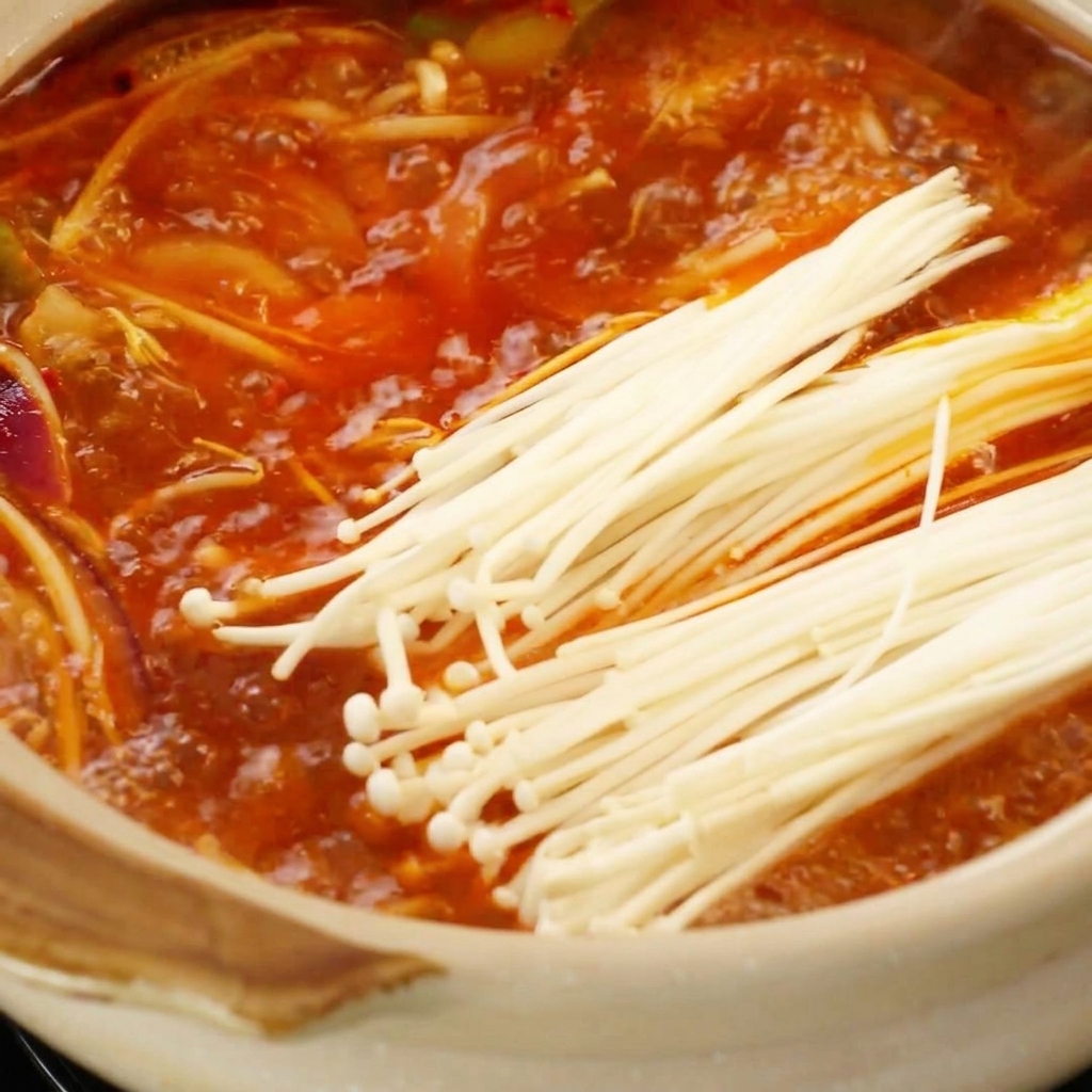 Setas enoki frescas colocadas en un caldo rojo burbujeante en la cazuela.
