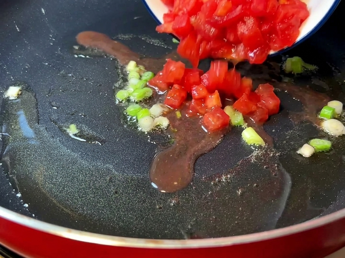 Tomates troceados cocinándose en una sartén hasta quedar suaves y jugosos.