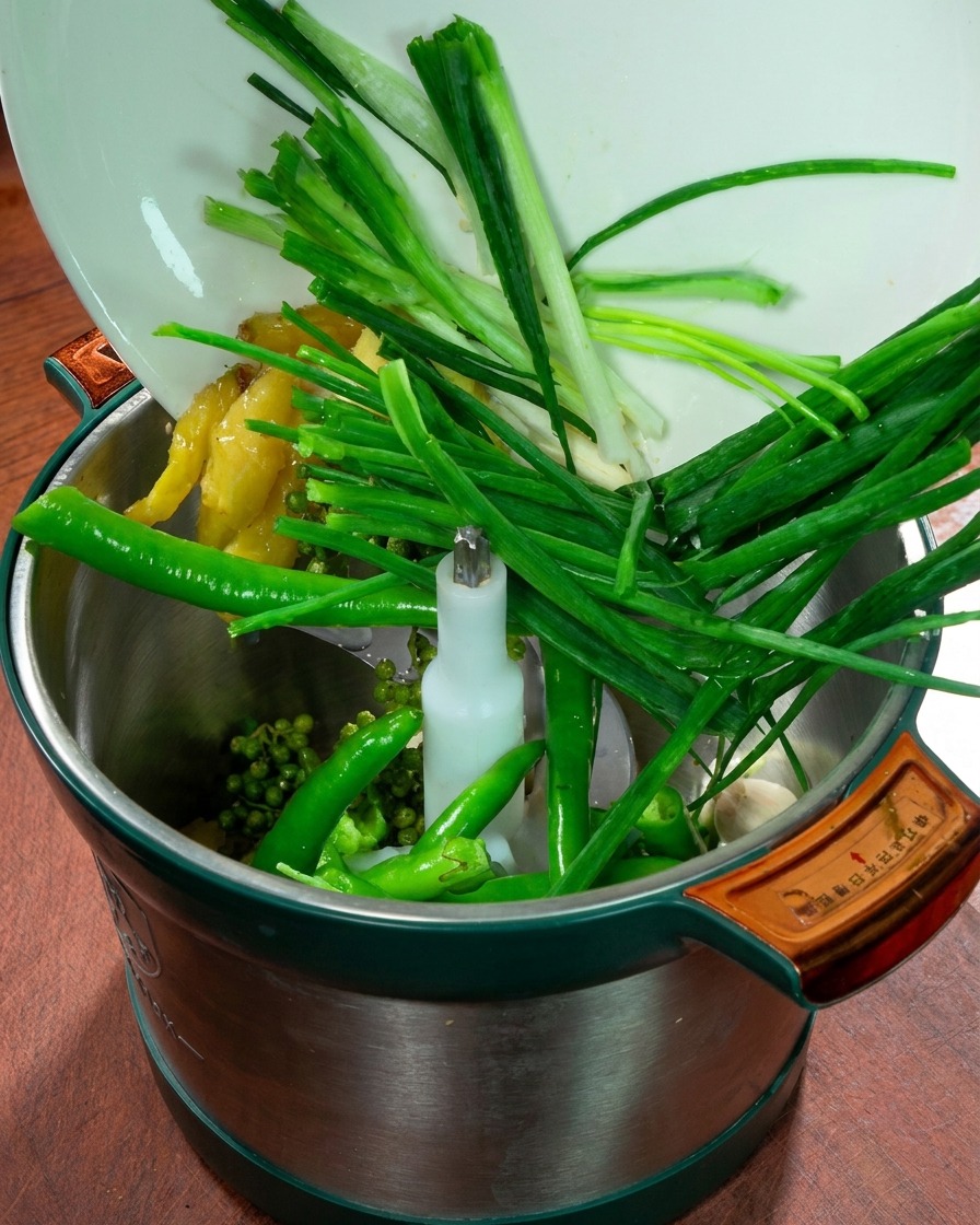 Un procesador de alimentos con cebolletas, jengibre, ajo, chiles verdes frescos y pimienta de Sichuan.