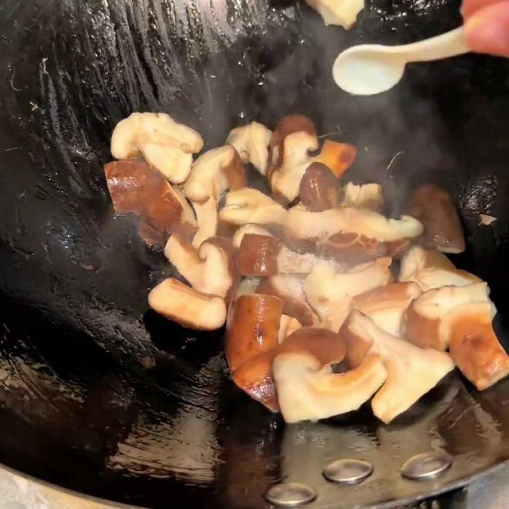 Sazonando las setas shiitake en un wok con sal y salsa de soja usando una cuchara pequeña.