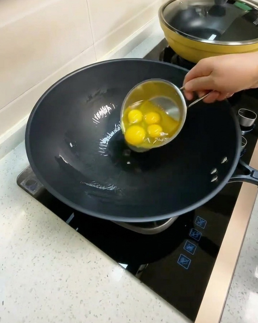 Cuatro huevos crudos siendo quebrados en un wok con aceite caliente.