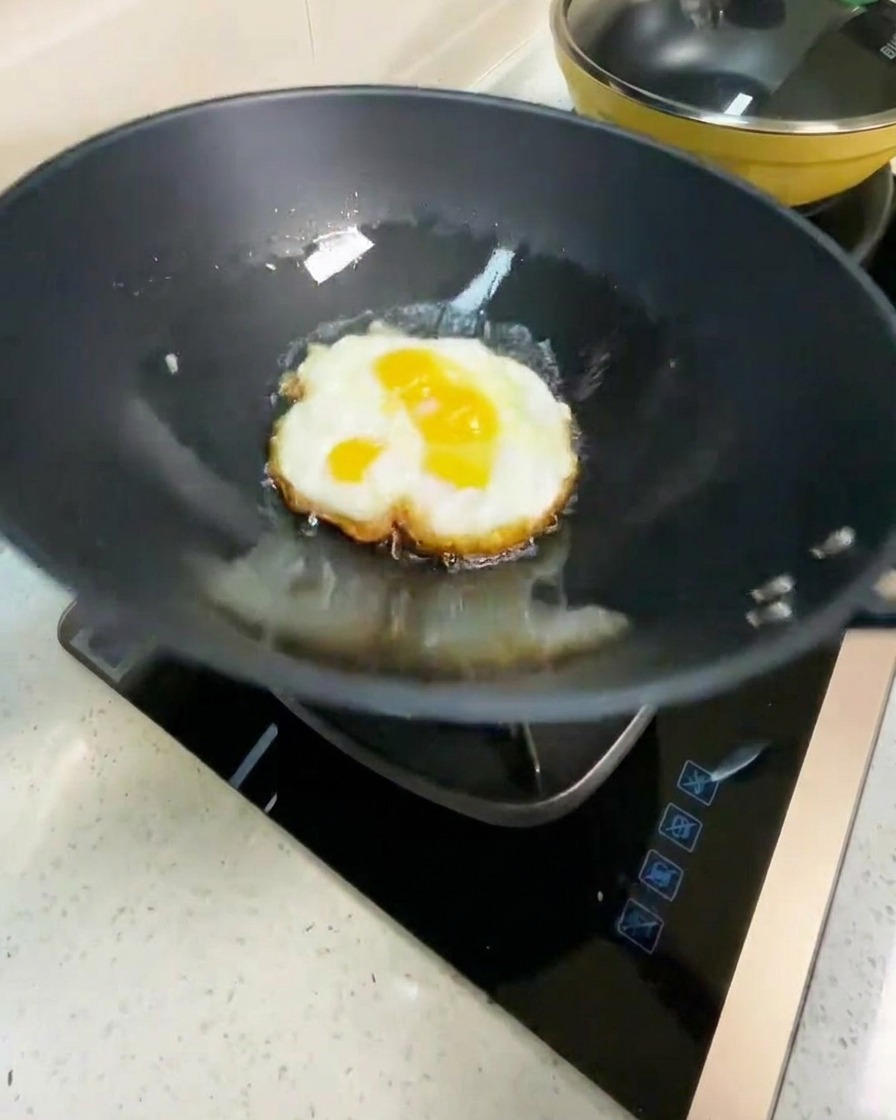 Huevo frito siendo volteado en un wok caliente, mostrando la parte inferior dorada.