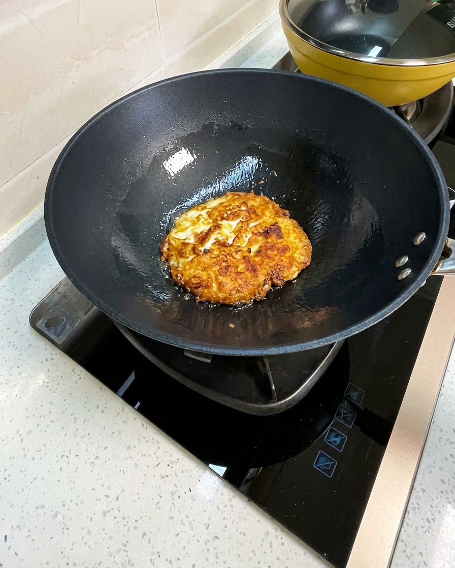Huevos fritos en un wok siendo troceados en pedazos grandes con una espátula de metal.