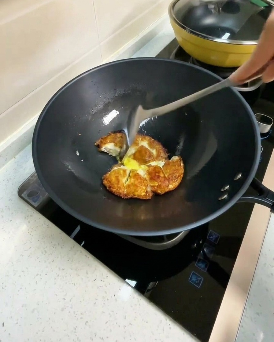 Agua caliente siendo vertida en un wok con trozos de huevo frito.