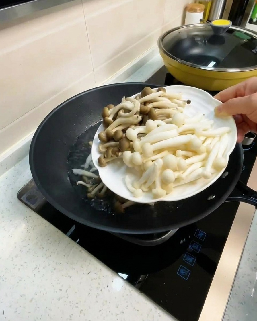 Un plato de setas de haya y setas sabor cangrejo siendo añadidas a un wok con caldo hirviendo.