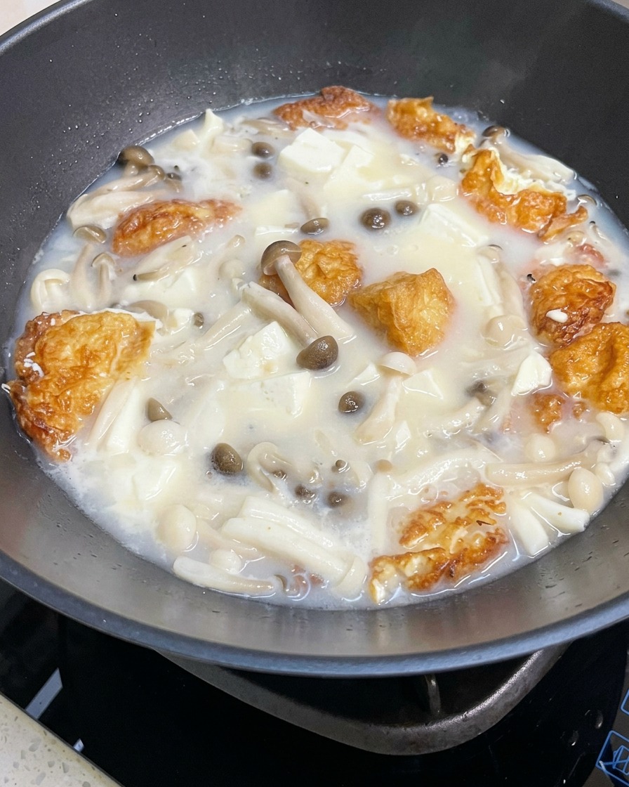 Primer plano de la sopa de setas y tofu hirviendo, siendo sazonada con sal y pimienta.