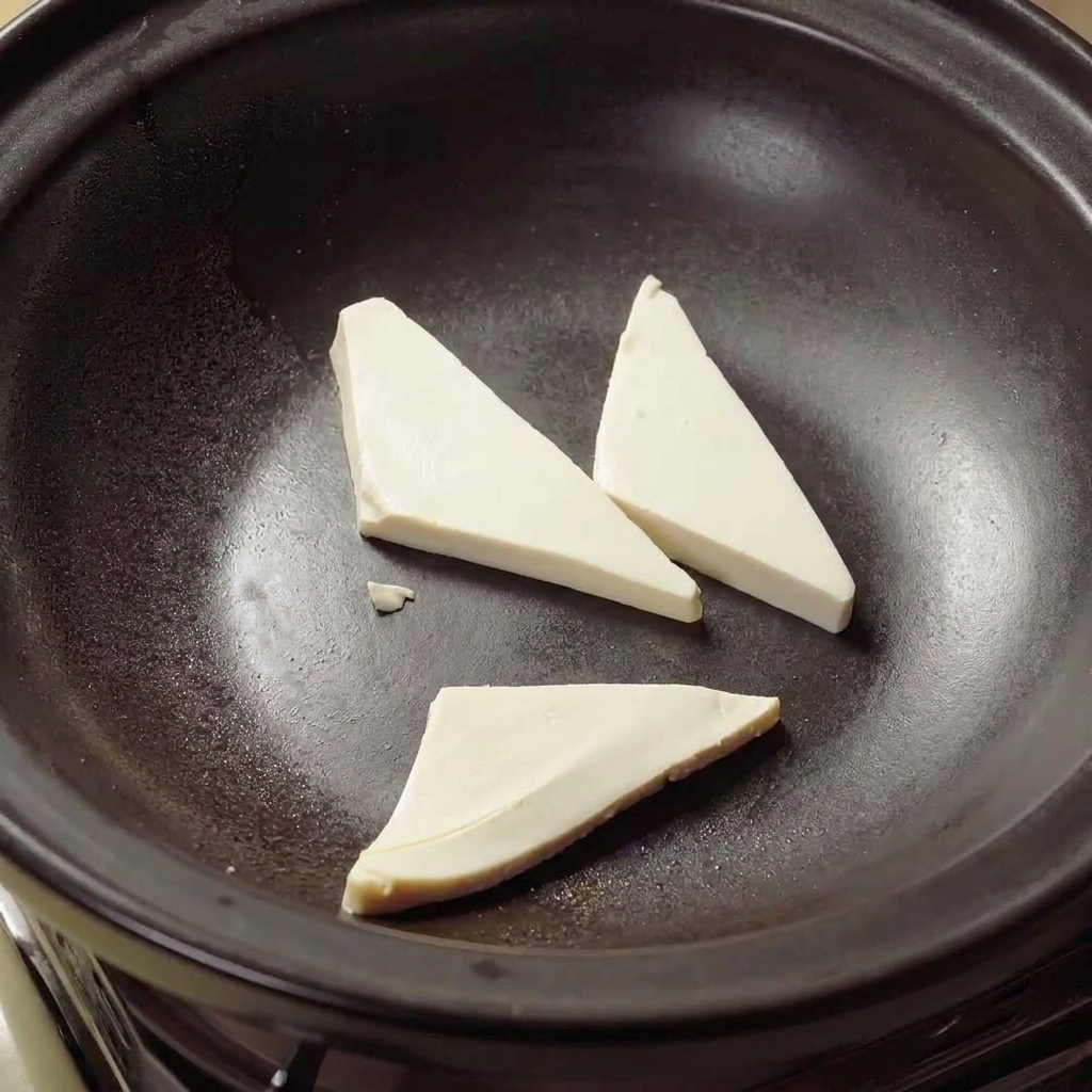 Triángulos de tofu friéndose en aceite caliente dentro de una cazuela de barro hasta que estén dorados.