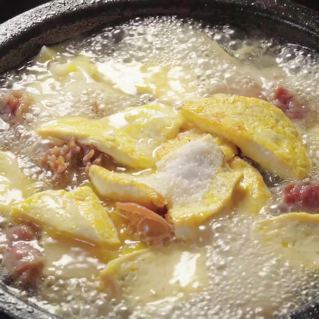 Condimentos siendo mezclados en una olla burbujeante de sopa de tofu y setas.