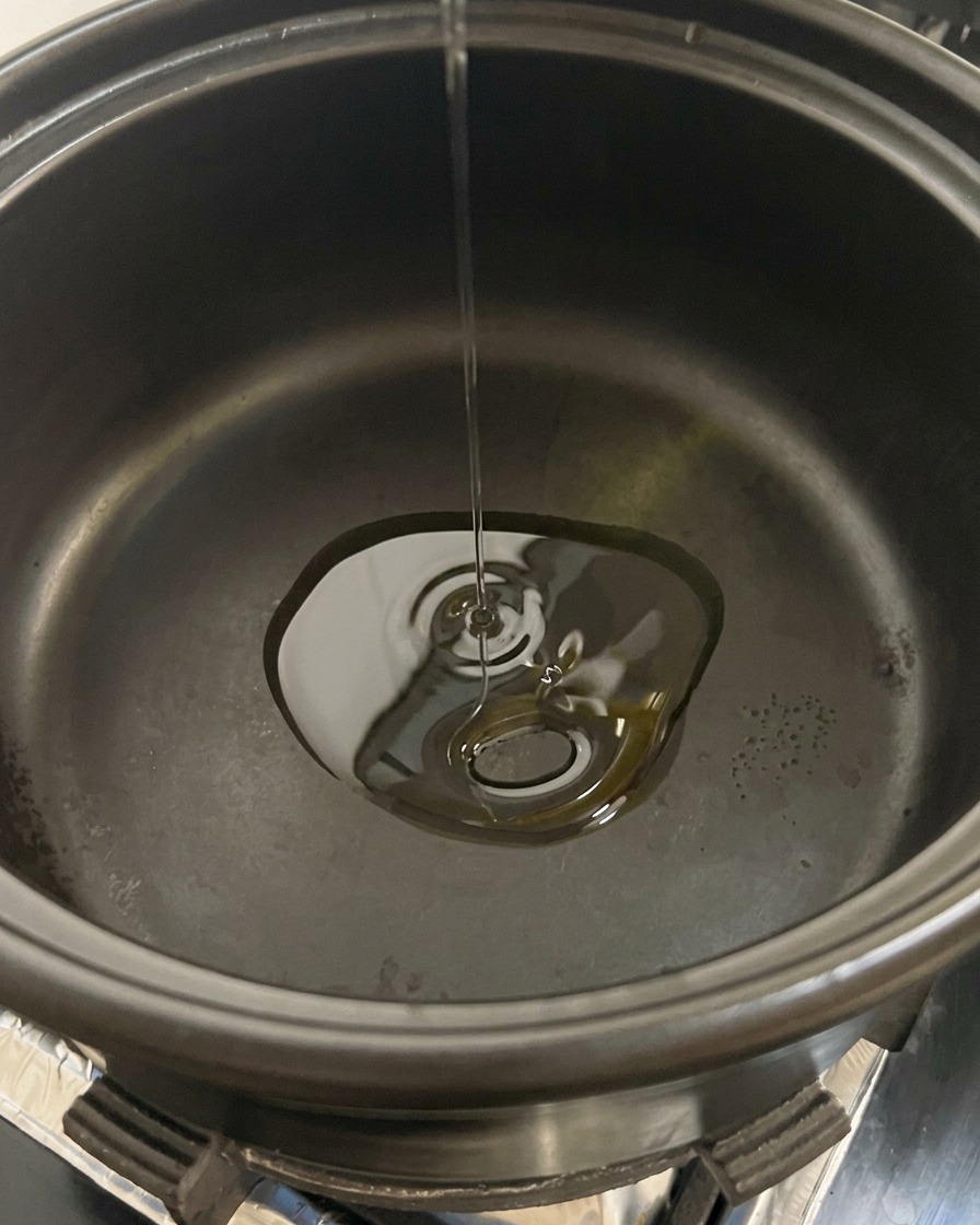 Champiñones blancos en rodajas siendo echados en una olla negra que contiene aceite caliente.