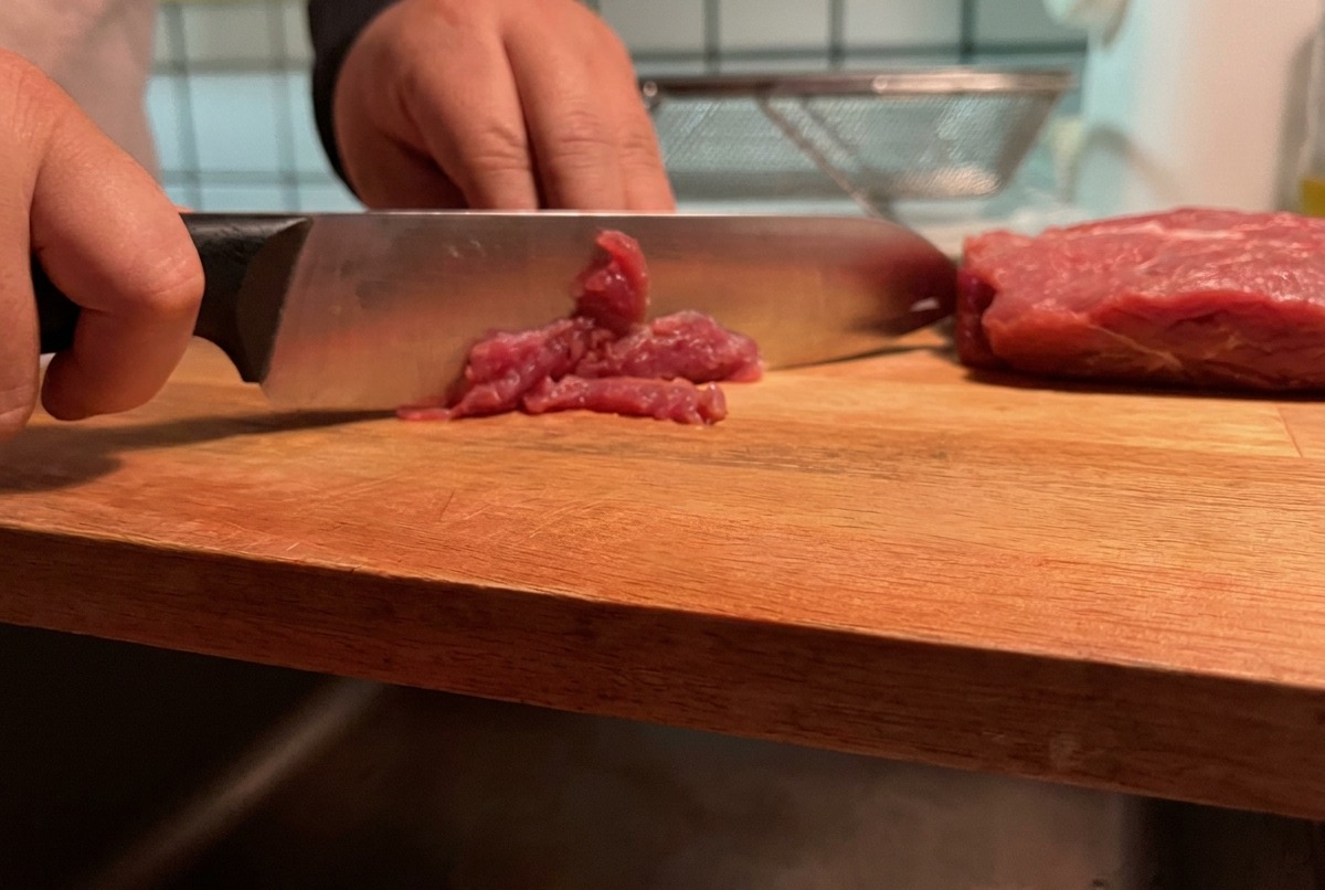 Cerdo magro siendo cortado en tiras finas sobre una tabla de cortar de madera.