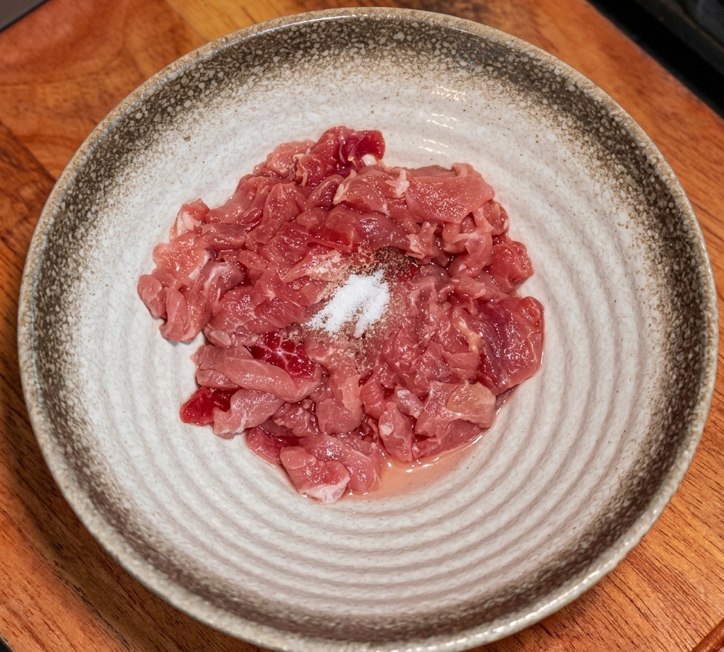 Tiras de carne cruda en un bol con varios condimentos y almidón espolvoreado encima.