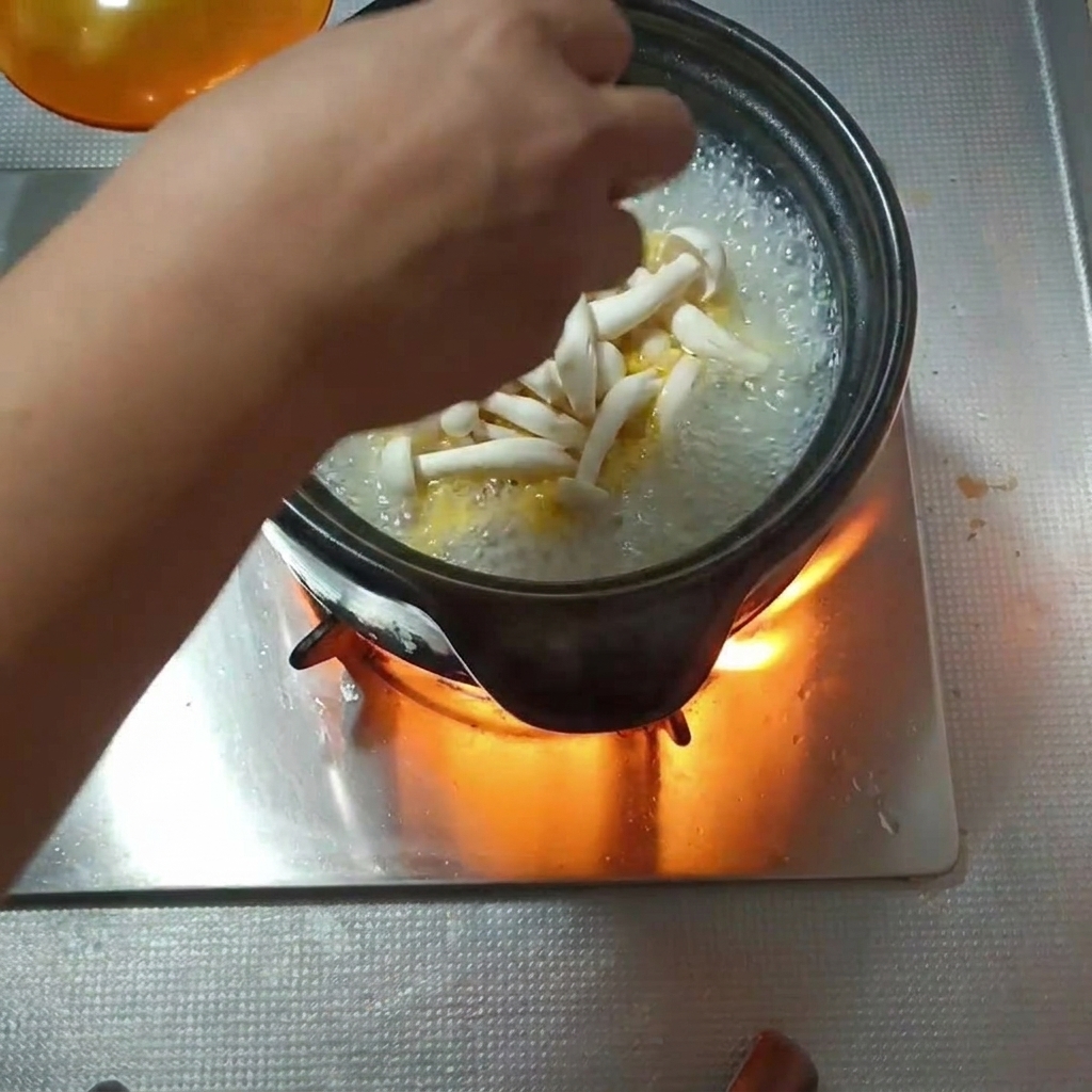 Varios tipos de champiñones siendo añadidos a una olla de barro burbujeante.