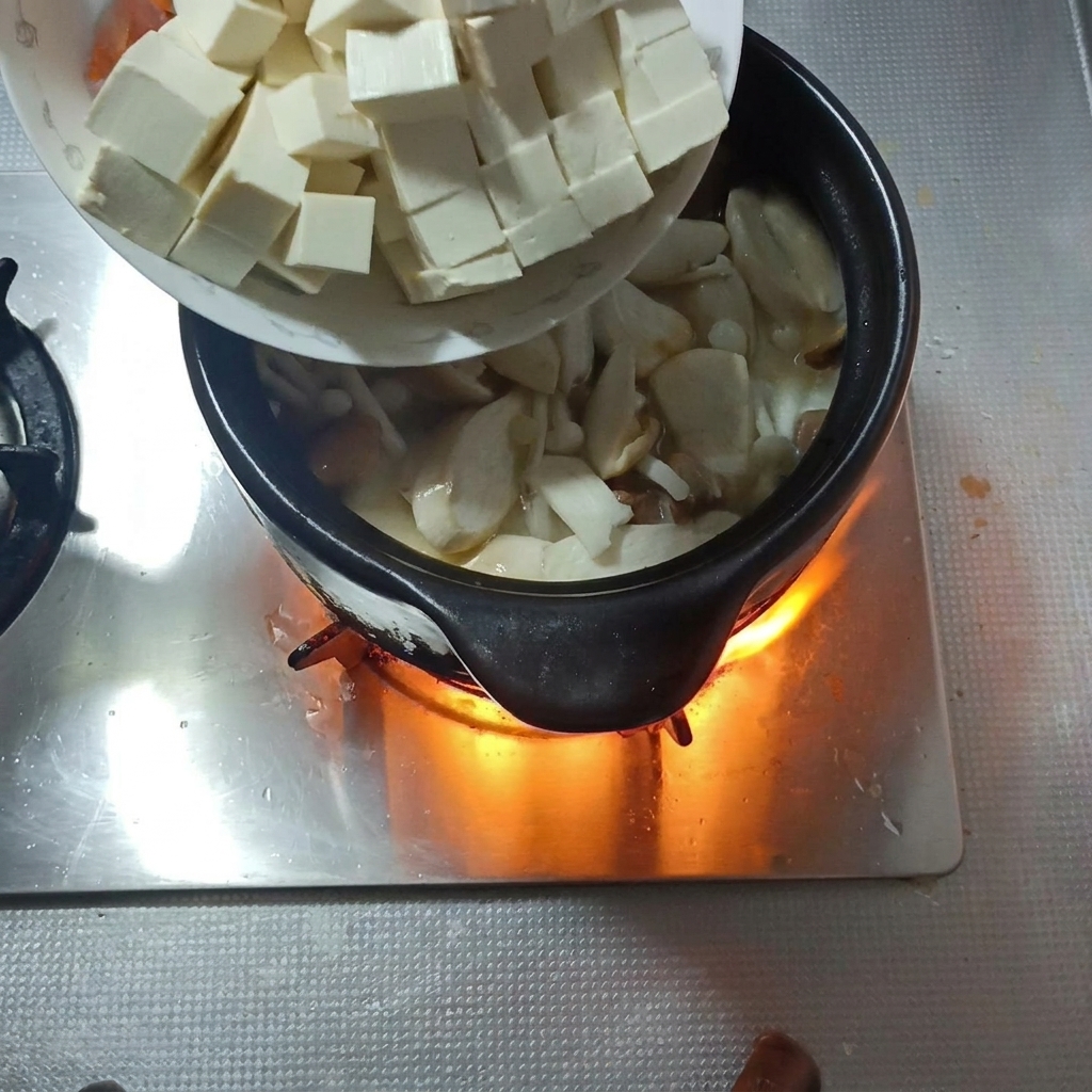 Dados de tofu suave y rodajas de zanahoria siendo añadidos a la sopa de champiñones.