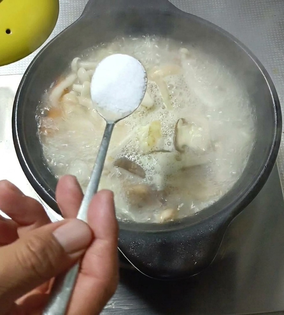 Primer plano de una cucharada de condimento siendo añadida a una olla de sopa de champiñones y huevo.
