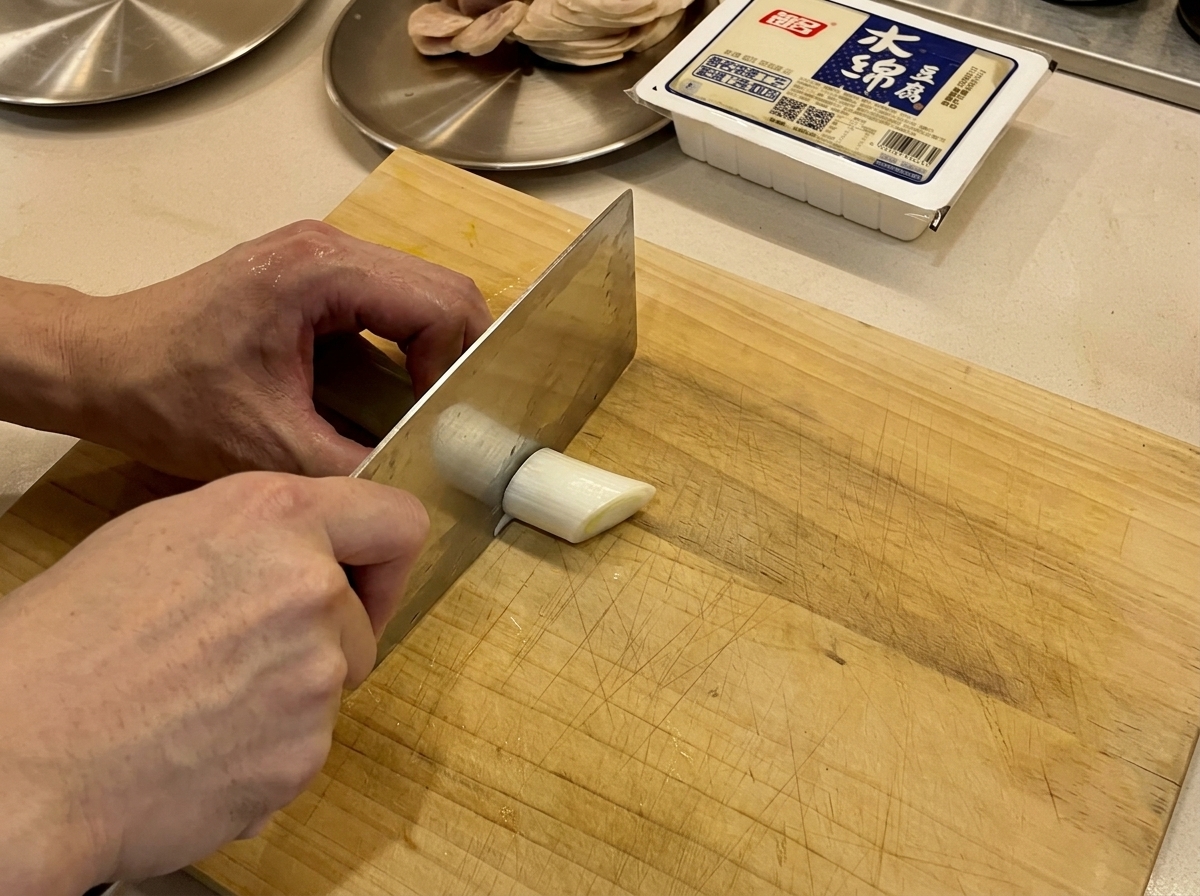 Cebollinos frescos siendo cortados sobre una tabla de madera con un cuchillo.