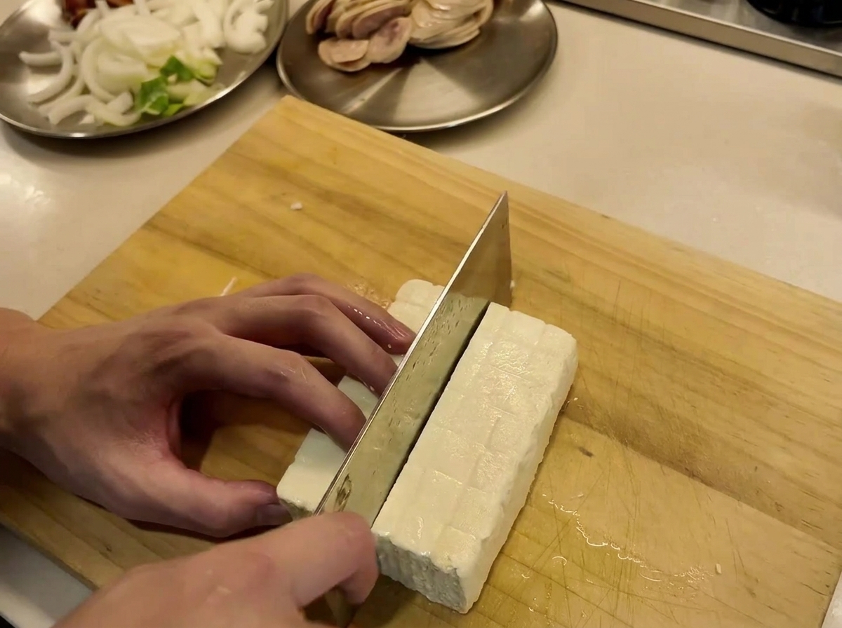 Bloque de tofu siendo cortado en rodajas uniformes sobre una tabla de madera.