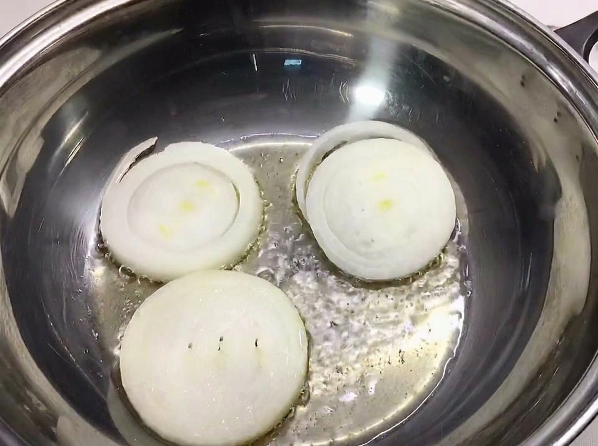 Tres rodajas gruesas de cebolla blanca colocadas en el fondo de una olla de acero inoxidable.