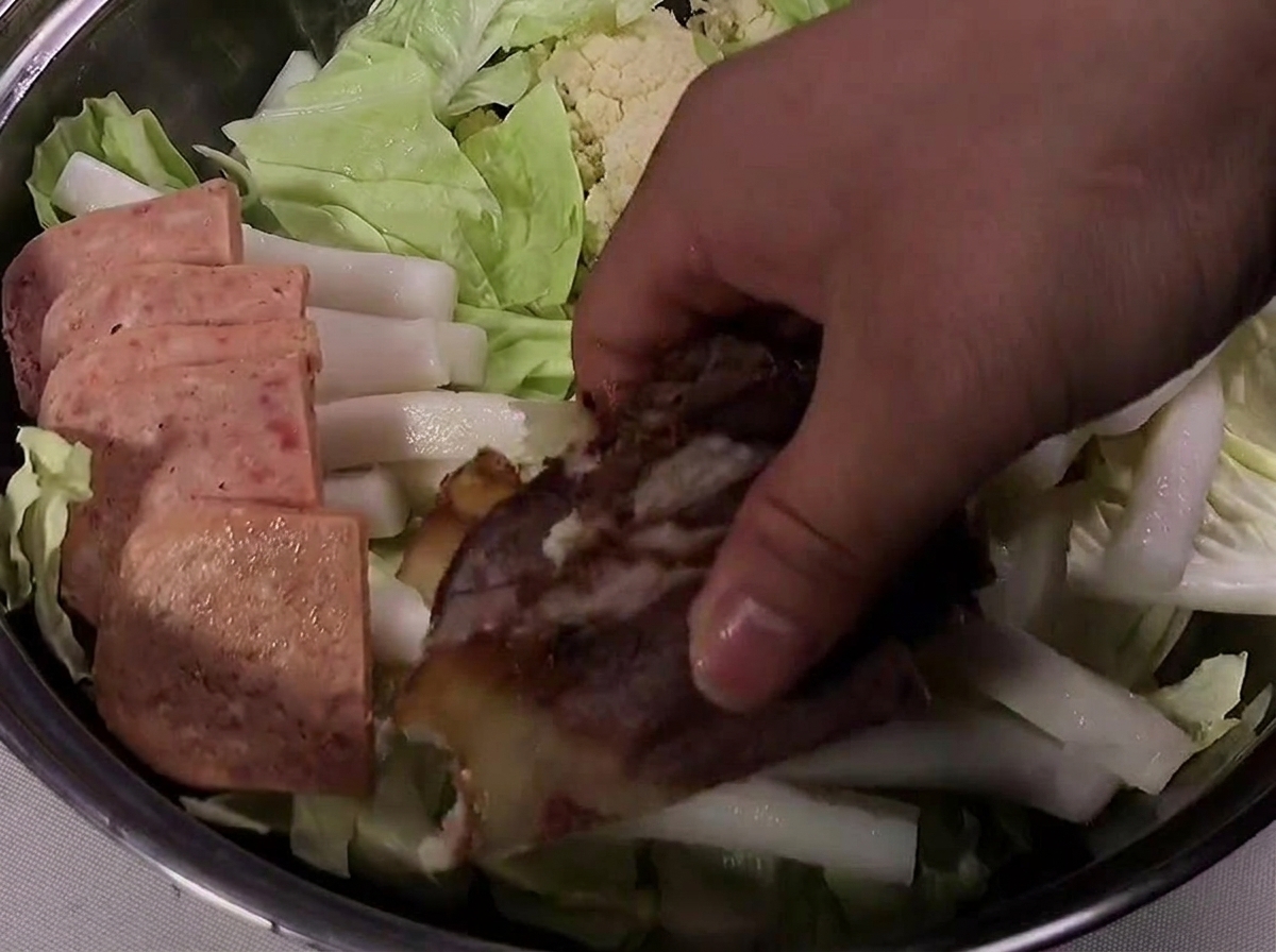 Rodajas de Spam, carne de res cocida y salchicha dispuestas ordenadamente alrededor del borde de la olla.