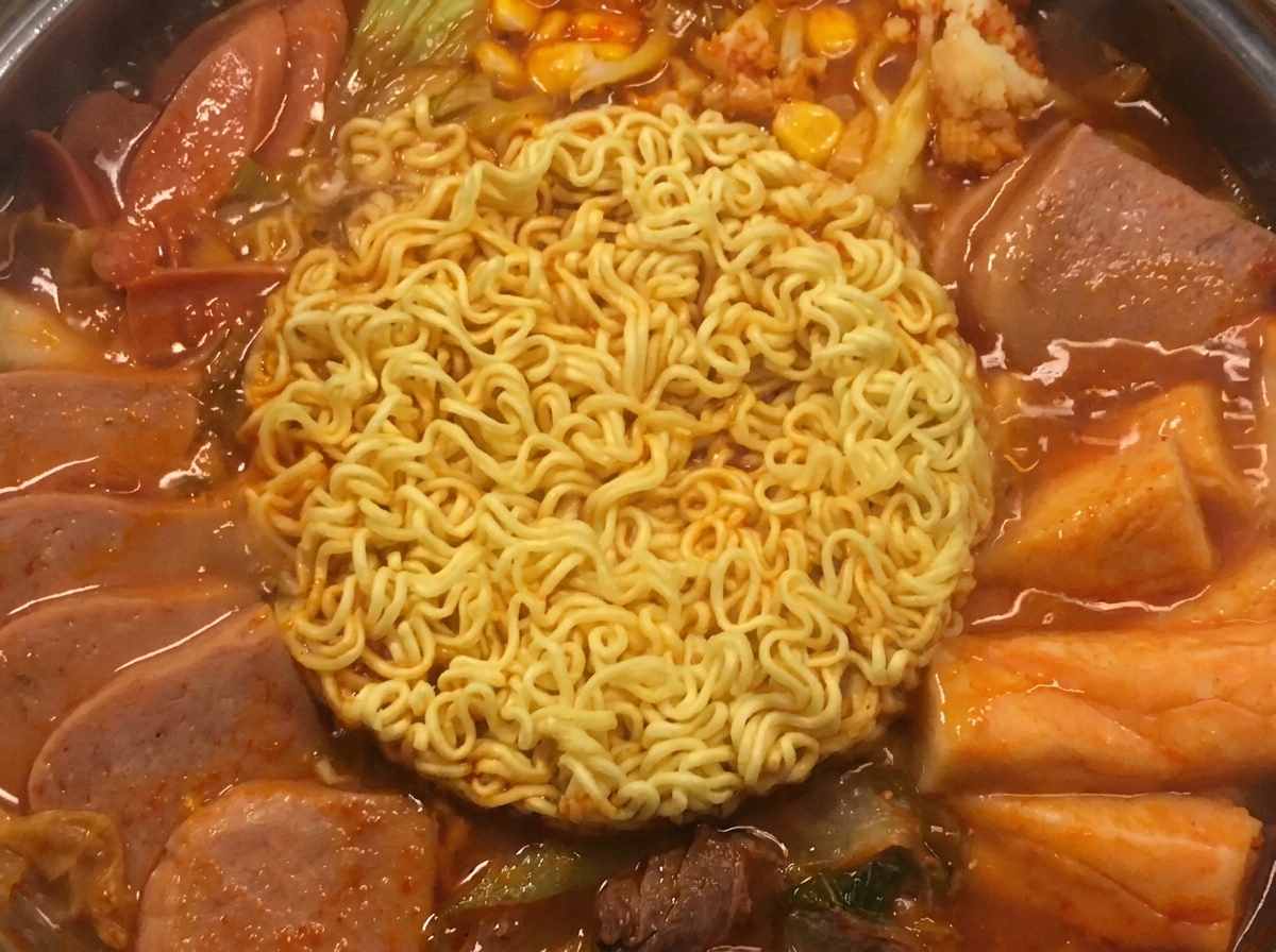 Dos cuadrados de queso amarillo dorado derritiéndose suavemente sobre los fideos ramen cocidos en la olla.