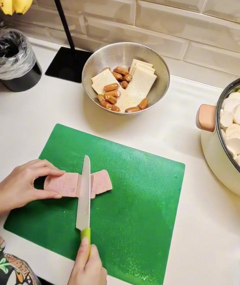 Rodajas de carne enlatada y pasteles de pescado dispuestos en una tabla, mostrando la preparación de los ingredientes principales.