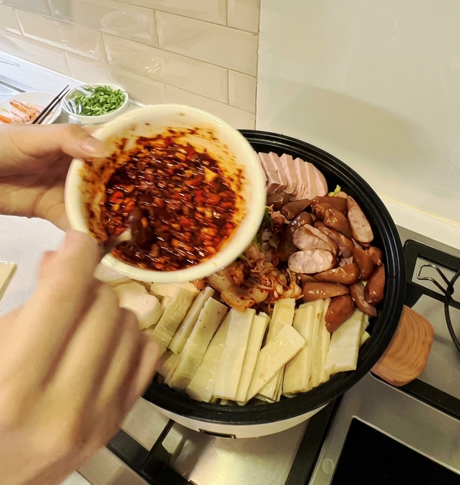 Un bol de vibrante salsa picante roja vertiéndose sobre la colorida disposición de ingredientes en una gran olla de estofado.