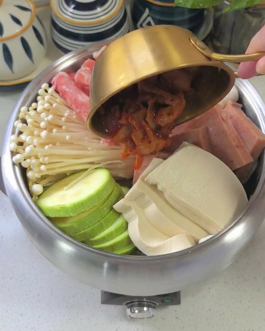 La salsa roja espesa siendo vertida desde un bol sobre los ingredientes dispuestos dentro de la olla.