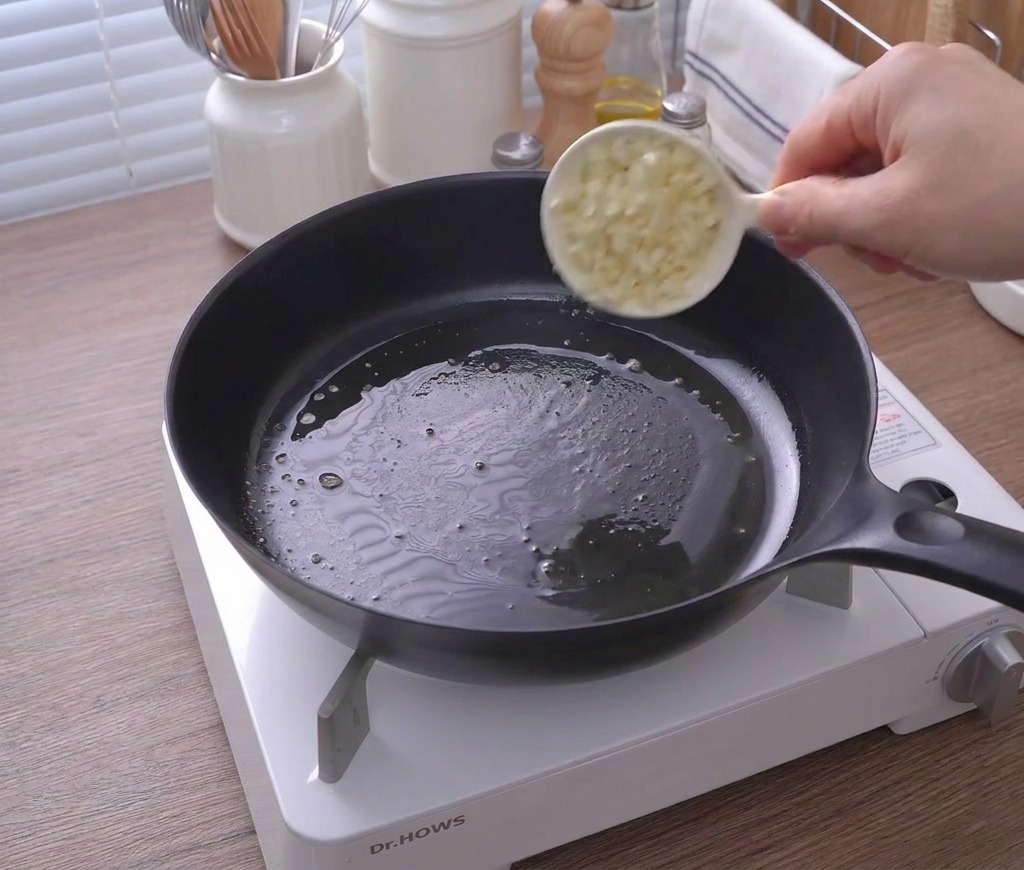 Ajo picado vertiéndose desde una taza blanca a una sartén con mantequilla derretida.