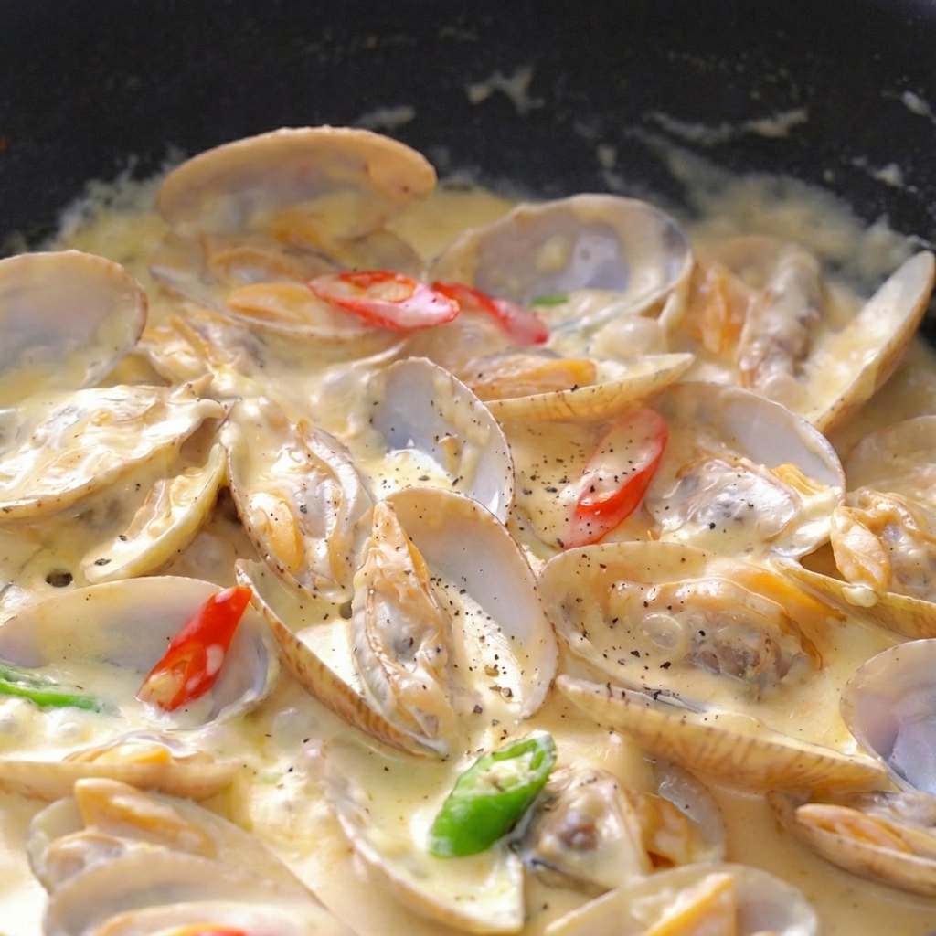 Primer plano de almejas en salsa espesa con pimienta negra, perejil y rodajas de chile.