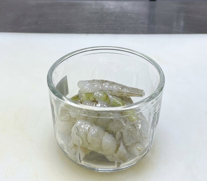 Camarones crudos translúcidos en un vaso de batidora sobre una tabla de cortar blanca limpia.