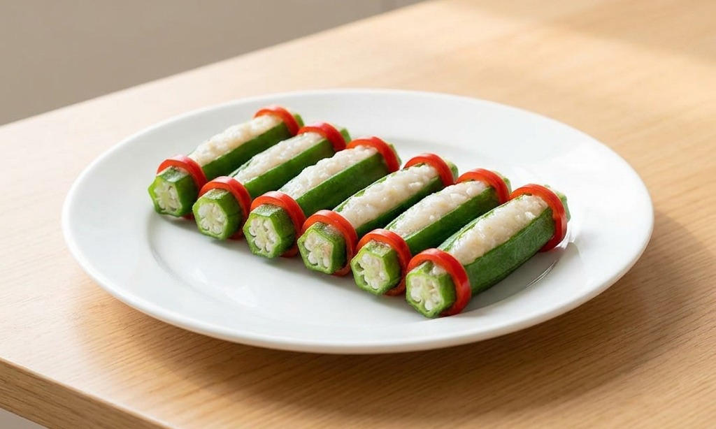 Plato blanco con una fila de okras rellenas de pasta de camarón, cada una decorada con dos aros de chile rojo brillante.