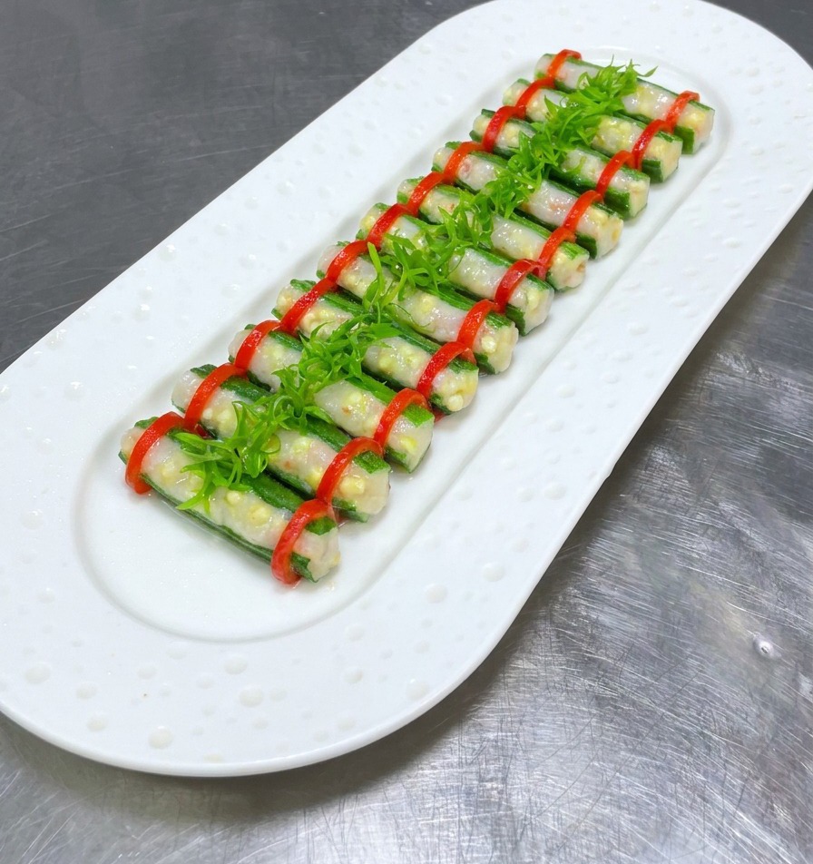 Okra rellena al vapor en un plato blanco coronada con una hilera central de tiras de cebolleta verde brillante.