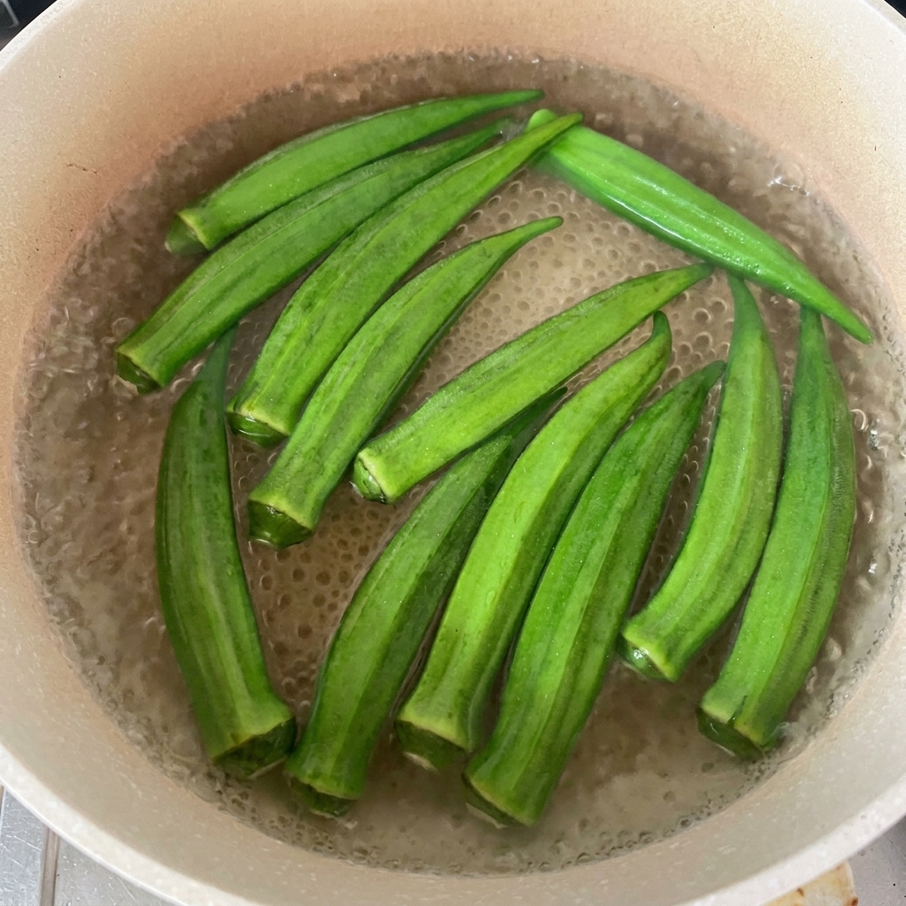 Vainas de okra verde fresca flotando en una olla con agua hirviendo.