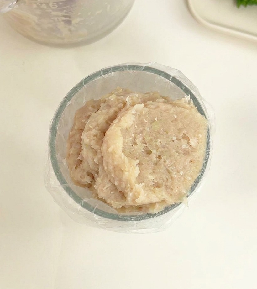 Un bol transparente que contiene una pasta de carne suave y clara con una manga pastelera de plástico lista para usar.