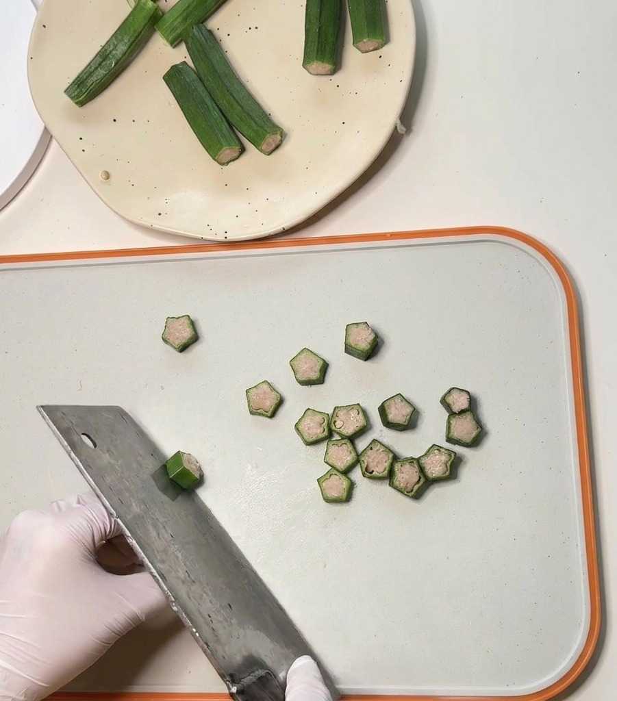 Un cuchillo grande cortando vainas de okra rellenas de pollo para formar pequeños premios redondos en forma de estrella.