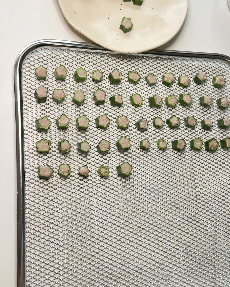 Docenas de premios de okra y pollo en forma de estrella colocados en filas ordenadas sobre una bandeja de malla metálica para deshidratar.
