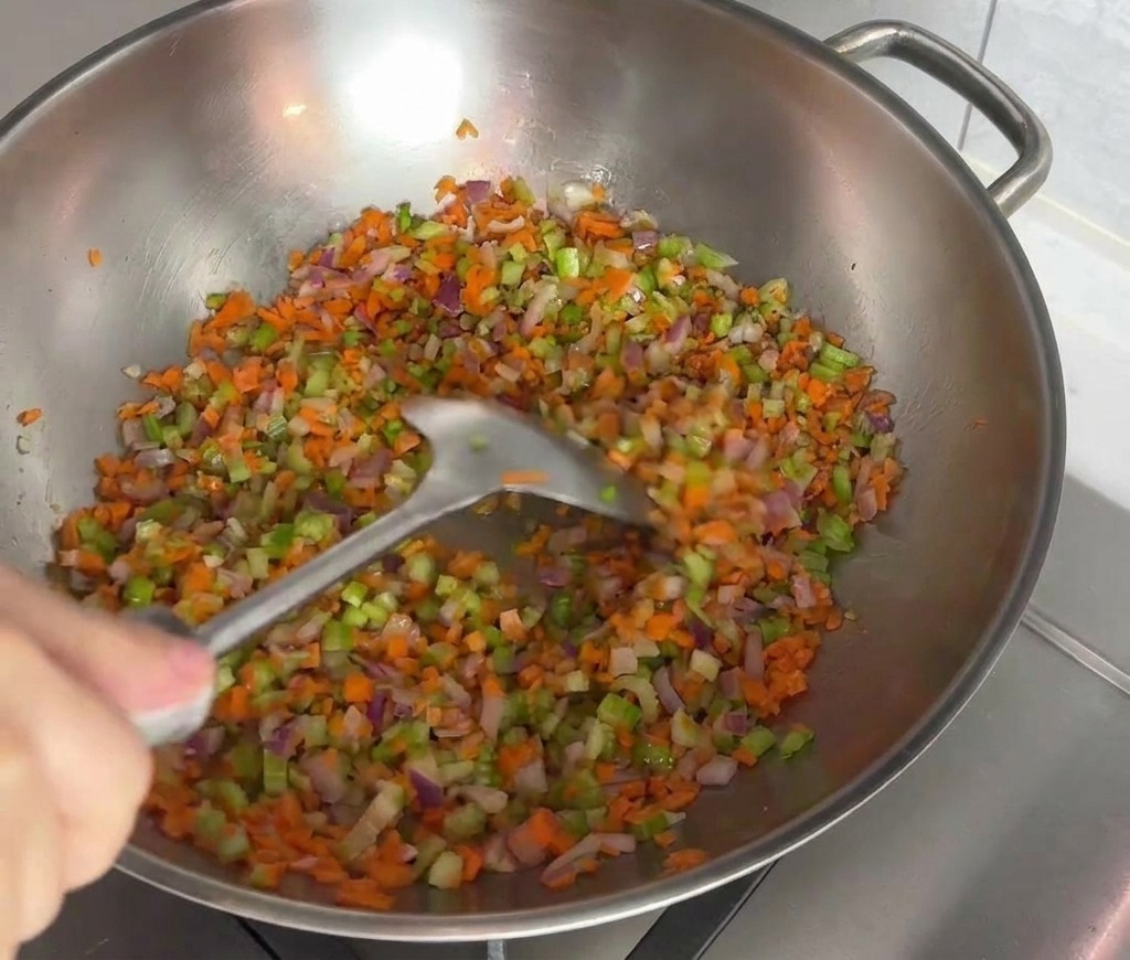 Mezcla colorida de zanahoria, apio y cebolla roja salteándose con una espátula en un wok de acero.