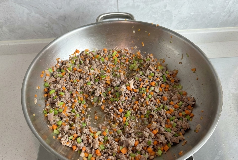 Carne picada salteándose con zanahoria y apio en un wok grande, con la carne bien dorada.